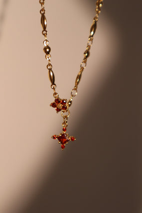 Gold-plated cross necklace with rich garnet-toned zirconia gemstones on a fine chain