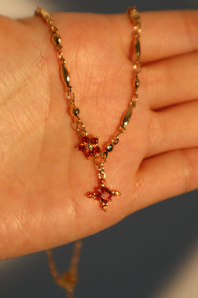 Gold-plated cross necklace with rich garnet-toned zirconia gemstones on a fine chain