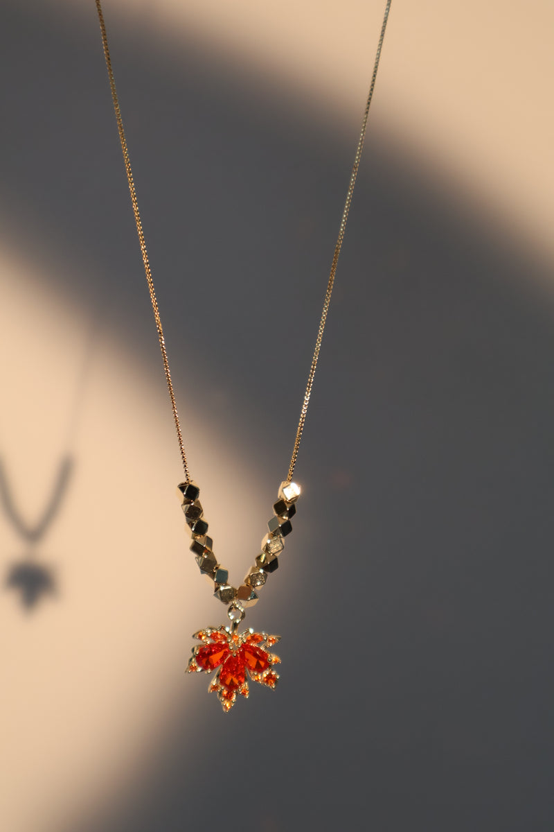 Gold-plated maple leaf pendant necklace with a red zirconia stone on a fine chain